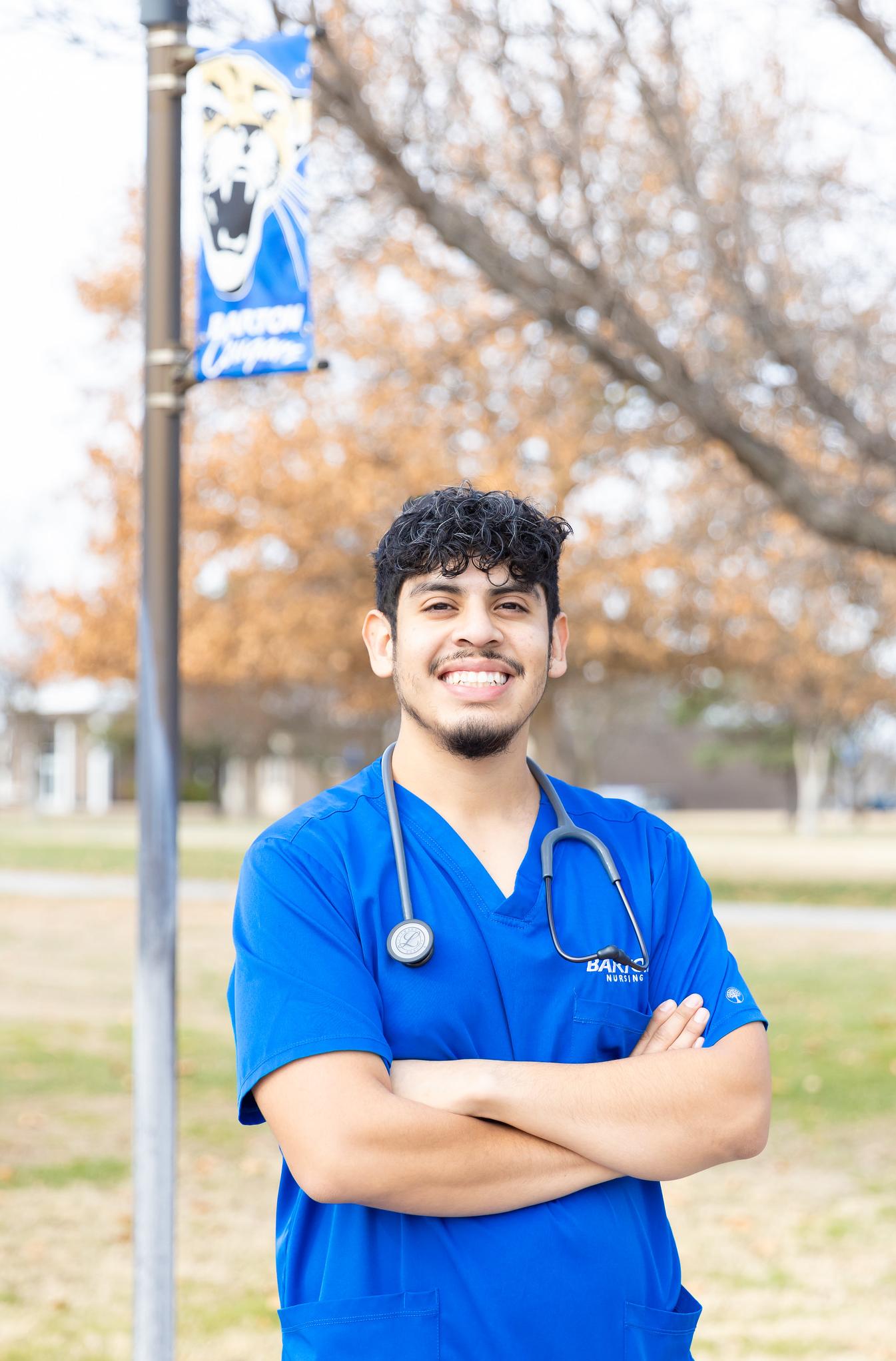 man in blue scrubs with arms crossed with barton flag in background